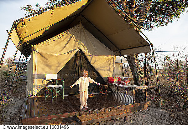 A five year old boy standing outside a tent arms outstretched  yawning. yawning outside tent  Kalahari Desert  Makgadikgadi Salt Pans  Botswana