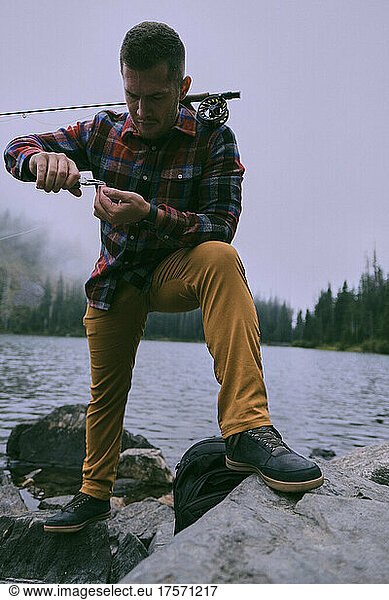 A flannel dressed fly fisherman changes a fly while fishing Lake 22.