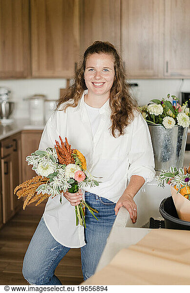 A florist standing in her kitchen holding a bouquet of flowers f