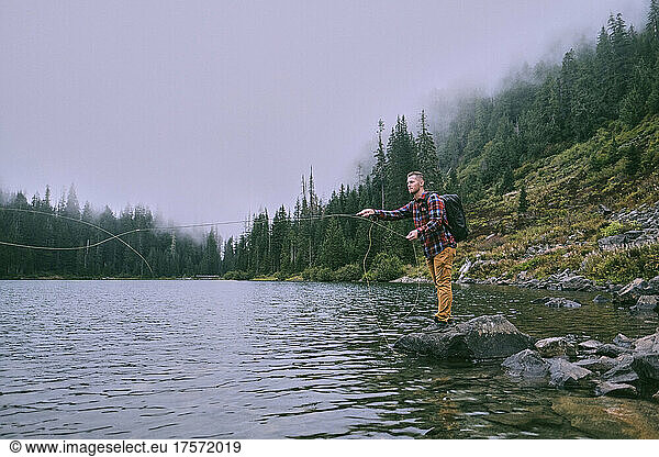A fly fisherman standing on a boulder makes a cast into Lake 22.