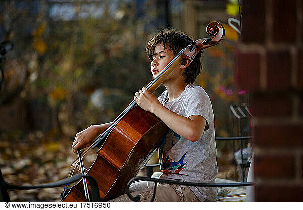 A focused boy plays cello outside in autumn