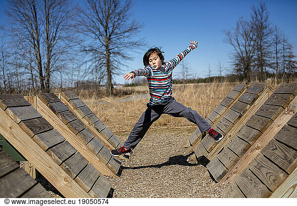 A focused child leaps across a series of wooden ramps in outdoor park