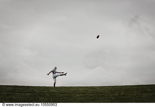 A football player in uniform  side view  practicing his kicking. Ball in mid air.