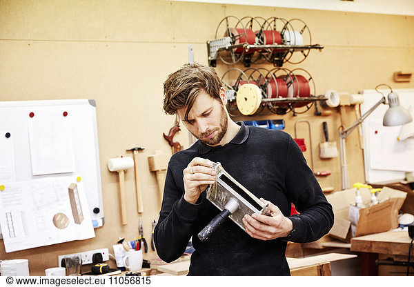 A furniture workshop. A young man holding an object and examining it closely.