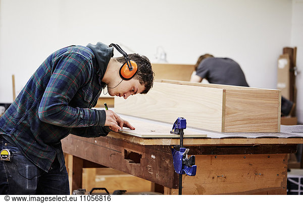 A furniture workshop making bespoke contemporary furniture pieces using traditional skills in modern design. A man marking a piece of wood with a pencil.