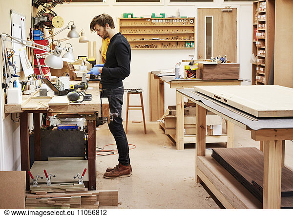 A furniture workshop making bespoke contemporary furniture pieces using traditional skills in modern design. A man standing at a workbench holding and examining an object.