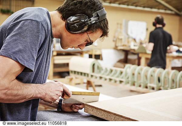 A furniture workshop making bespoke contemporary furniture pieces using traditional skills in modern design. A man using a small handsaw to trim wood.