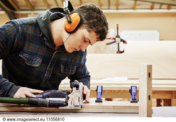 A furniture workshop making bespoke contemporary furniture pieces using traditional skills in modern design. A young man using tools to shape a piece of wood.