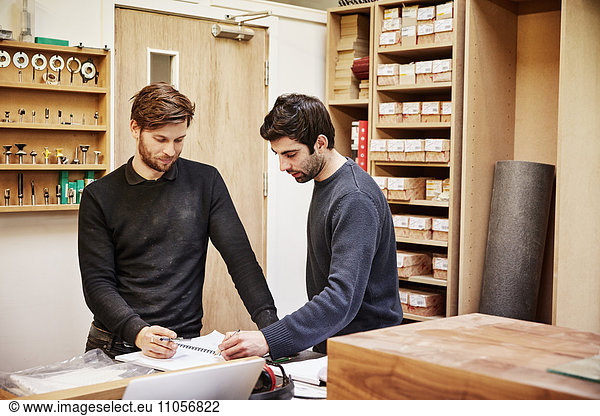 A furniture workshop making bespoke contemporary furniture pieces using traditional skills in modern design. Two people discussing a design  referring to drawings.