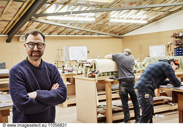 A furniture workshop making bespoke contemporary furniture pieces using traditional skills in modern design. Two people working and a man standing with arms folded.
