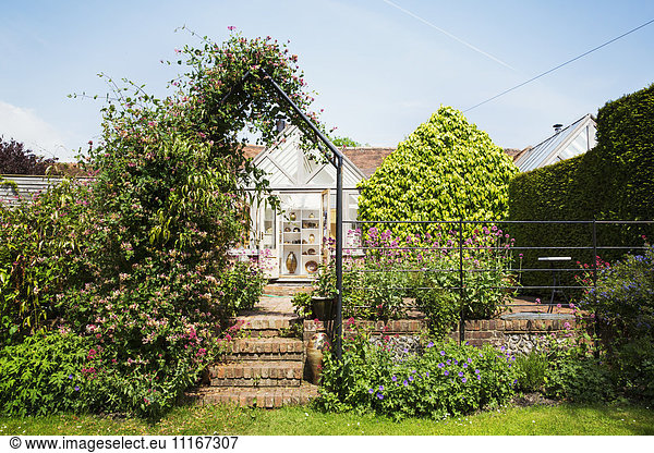 A garden pergola with climbing plants  and a historic house in a village.