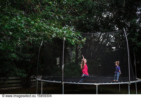 A girl and boy jump on an outdoor trampoline.