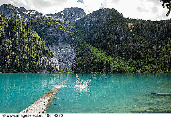 A girl does perfect back dive into the blue waters of Joffre Lakes
