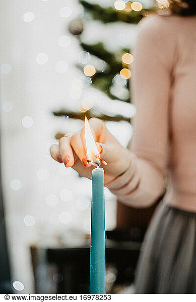 A girl in a festive outfit lights a candle on a festive table against the background of a Christmas tree on New Year's Eve