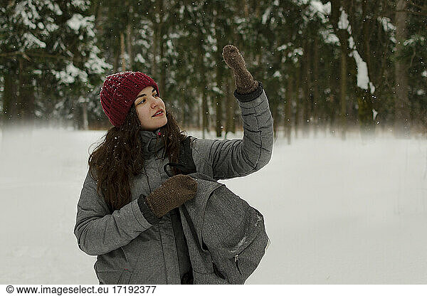 A girl in a red hat holds a backpack  looks at her hand  catches snow