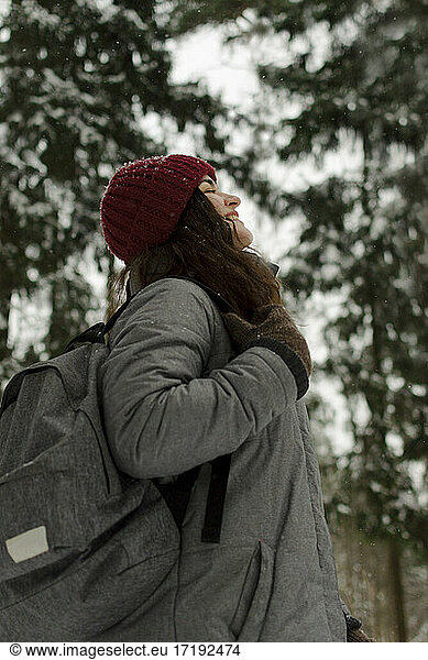 A girl in a red hat  looks at the sky  smiles  it is snowing  travel.