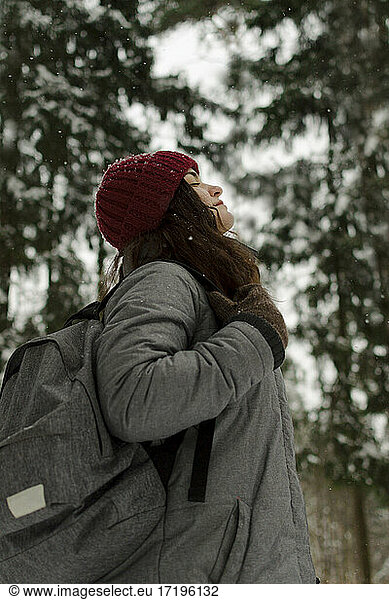 A girl in a red hat  looks at the sky  smiles  it is snowing  travel.