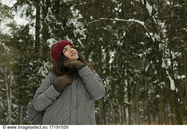 A girl in a red hat smiles  looks at the sky  smiles  it is snowing.