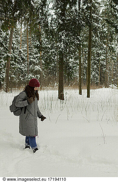 A girl in a red hat walks in the woods on a cloudy day  a lot of snow.