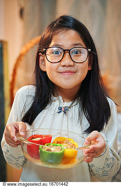A girl showing her cooked colorful bell peppers in the glass bowl