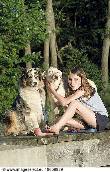 A girl sits with her two dogs on a deck.