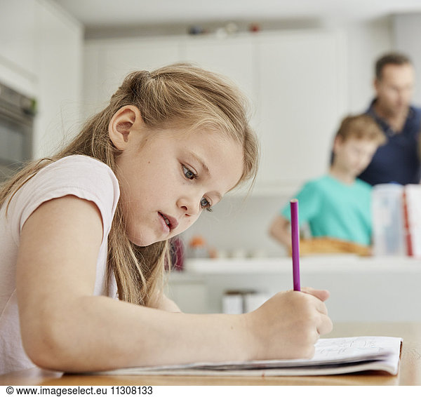 A girl sitting at a table in the family kitchen  holding a pencil  doing her homework.