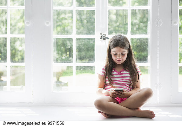 A girl sitting playing  holding a smart phone.