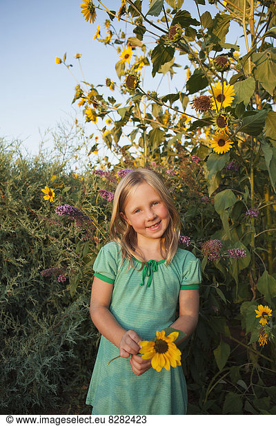 A Girl Standing Outside In A Garden  Holding A Large Sunflower.