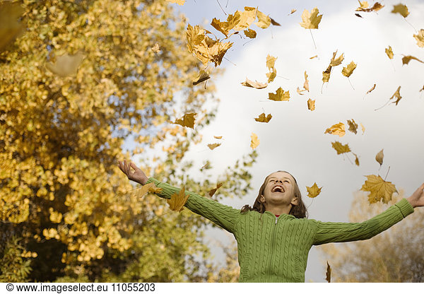 A girl throwing fallen autumn leaves into the air.