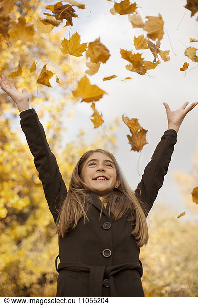 A girl throwing fallen autumn leaves into the air.