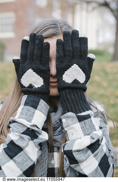 A girl wearing woolly gloves with a heart shaped design  hiding her face.
