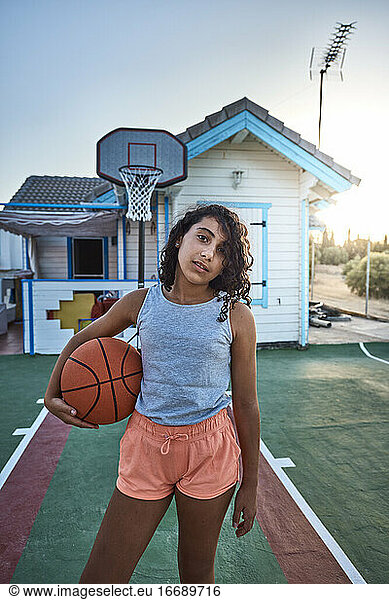 A girl with curly hair standing on the basketball court of her own home