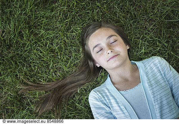 A girl with long hair fanned out  asleep on the grass.