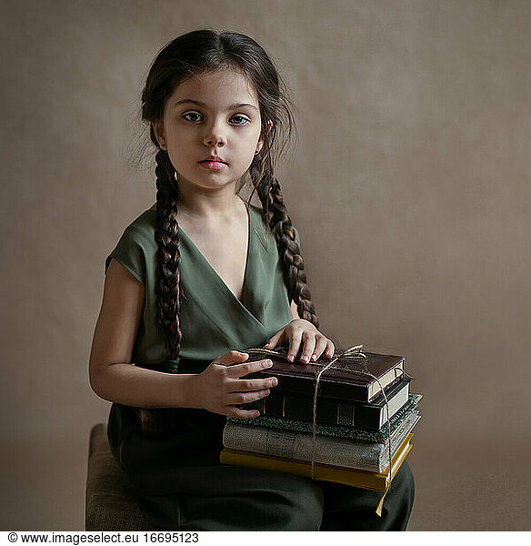 a girl with long pigtails sits and holds a stack of books in her lap