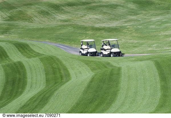 A golf course with mown fairways creating a pattern on an undulating landscape. Two electric golf buggies.
