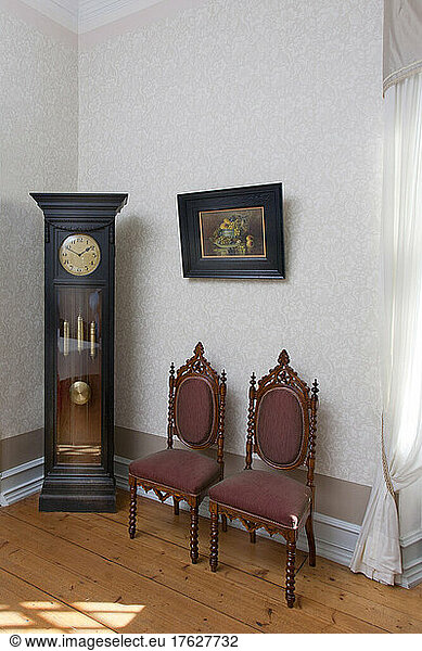 A grandfather clock and two chairs in a room in a hotel.