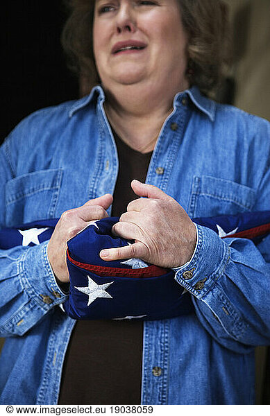 A grieving middle aged mother clutching a folded American flag.