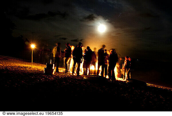 A group gathered around a campfire on the shore of Sebago lake.