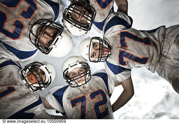 A group of football players  young people in sports uniform and protective helmets  in a team huddle viewed from below.