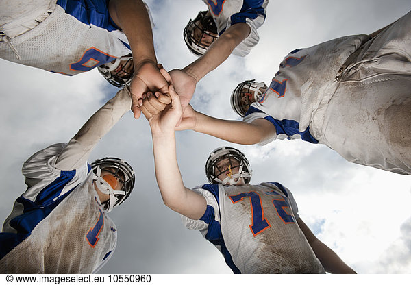 A group of football players  young people in sports uniform and protective helmets  in a team huddle viewed from below.