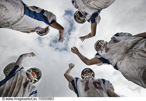A group of football players  young people in sports uniform and protective helmets  in a team huddle viewed from below.