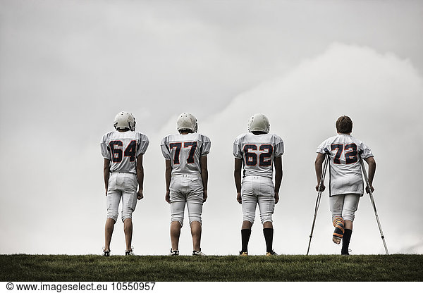 A group of football players  young people in sports uniform and protective helmets. One person using crutches.