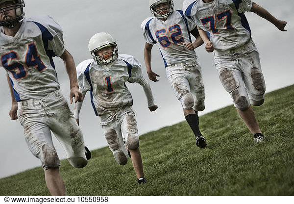 A group of four football players,  young people in sports uniform and protective helmets running forward.