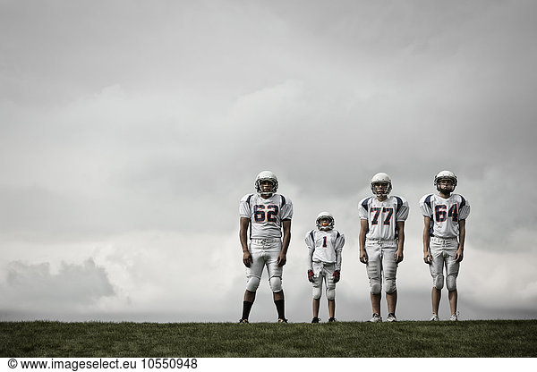 A group of four football players in sports uniform  three tall figures and one shorter team player.