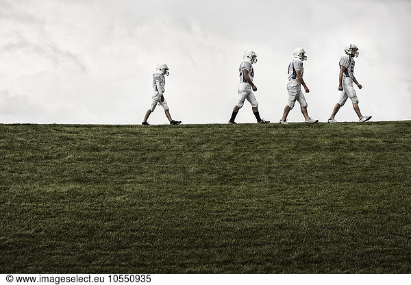 A group of four football players in sports uniform  three tall figures and one shorter team player lagging behind them.