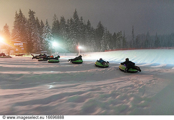 A group of people slide down a snowhilll on tubes in Oregon.
