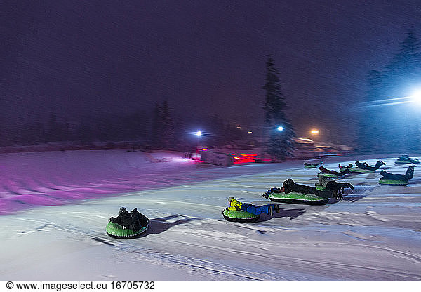 A group of people slide down a snowhilll on tubes in Oregon.
