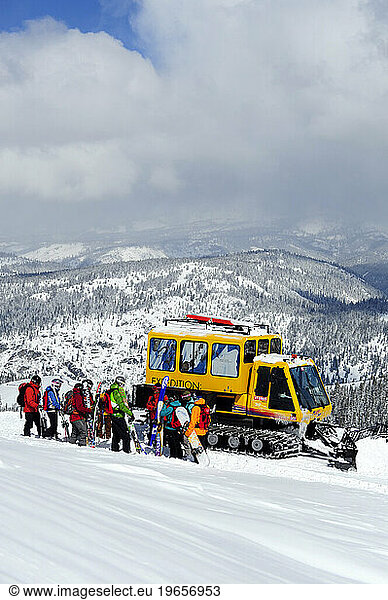 A group of skiers and snowboarders stand in front of a snow cat on a powder day while cat skiing at a mountain resort  California.
