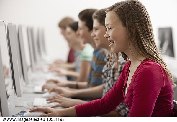 A group of young people  boys and girls  working at computer screens in class.