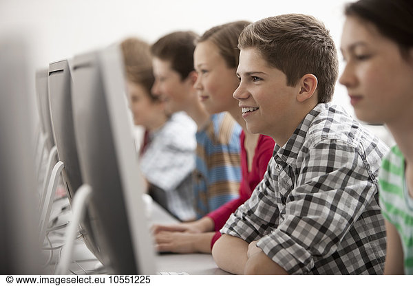 A group of young people  boys and girls  working at computer screens in class.